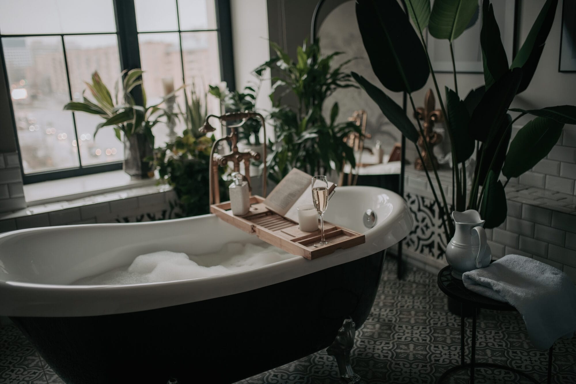 Native hues organic shapes look of bathroom with big window oval bathtub in neutrals earth tones. Green palm plants candles bubblebath leasure and relaxation skin selfcare wellness luxury living